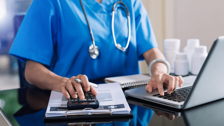 A person in scrubs sitting at a desk with a laptop