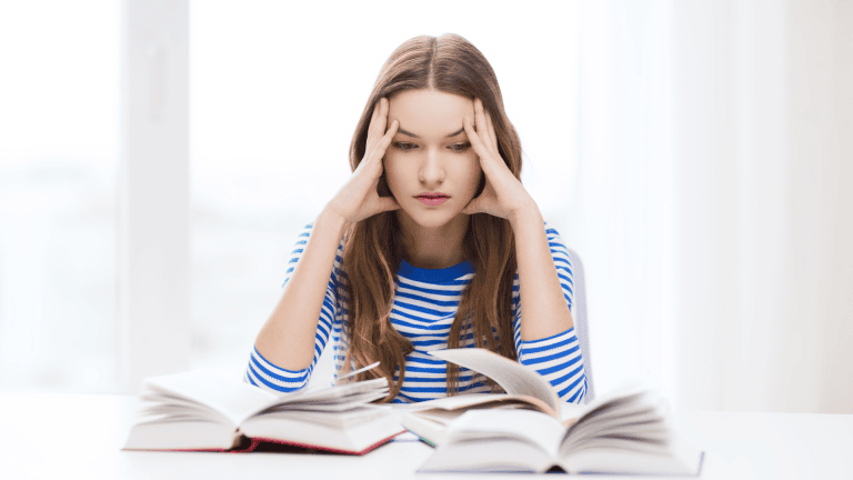 A person sitting at a desk with their head in their hands and a book in front of them.