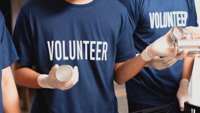 Individuals in navy volunteer shirts handling canned goods in a community service setting.