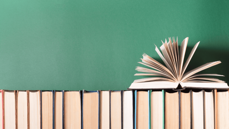 an open book on top of a stack of books in front of a green chalkboard